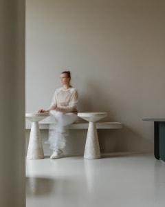 A modern concrete bench sitting against a plain wall, with a person seated on it.