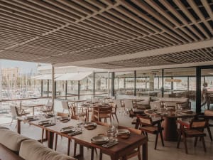 A modern restaurant interior with wooden tables and chairs, overlooking a marina.