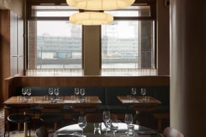Modern cafeteria interior with wooden tables and chairs, large windows, and industrial-style lighting.