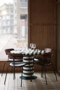 A modern dining setting with a striped table, metal-framed leather chairs, wooden walls, and large windows.