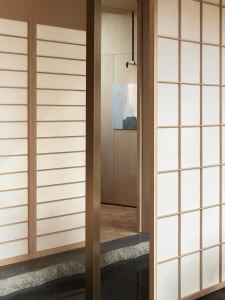 Modern minimalist interior space with wooden sliding doors and white panels, featuring a painting on the wall and a floor wit