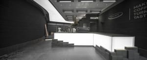A sleek, minimalist coffee shop interior with a concrete counter and geometric design elements.