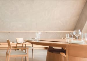 A minimalist dining room features wooden furniture including a table, chairs, and wine glasses.