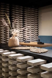 A coffee shop interior featuring industrial-style concrete stools arranged on a step-like platform with a vases containing dr