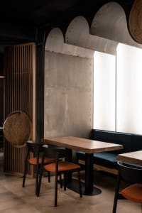 Modern restaurant seating area featuring wooden tables, concrete walls, and metal accents.