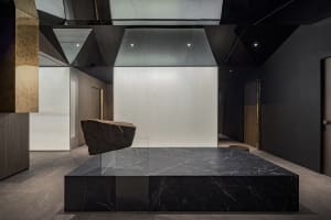 A modern lobby featuring a black marble platform and a black marble rock sculpture.