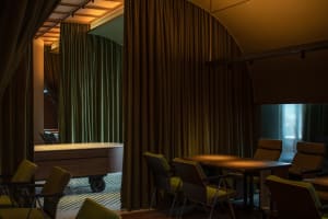 Industrially styled restaurant interior with green curtains, wooden tables, and metal chairs
