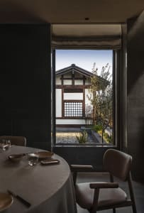 Modern restaurant with concrete floor, minimalist design, and a view of a traditional building through a window.