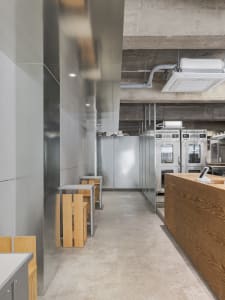 Industrial-style restaurant interior with metal walls, concrete flooring, and wooden tables and stools.