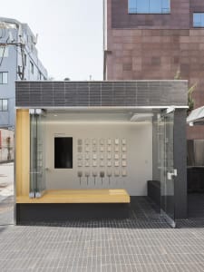 A modern exhibition space featuring a glass display case and various objects on a wooden platform.