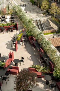 A modern outdoor cafe with concrete seating, metal tables, and glass railings.
