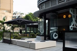 Modern restaurant exterior with metal accents, large glass windows, concrete seating, and green plants