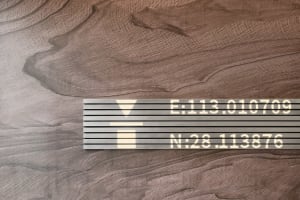 A minimalist building exterior featuring a wooden texture with a metal plaque displaying coordinates.