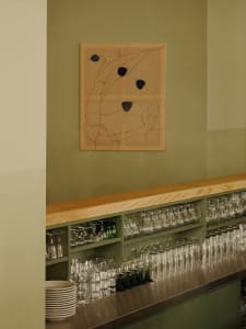 A minimalist bar counter with a wooden surface, featuring shelves stocked with glasses.
