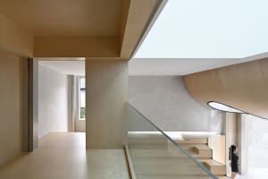 A modern residential staircase with wooden steps and railings, featuring a curved wooden wall and a skylight ceiling.