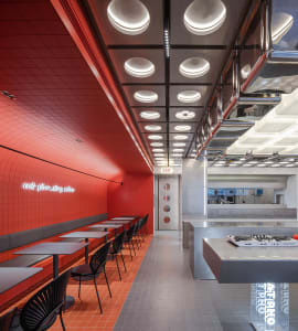 A modern restaurant interior with red tiled walls, black chairs, and white tables.