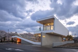 Modern exterior view of a house with white concrete walls, recessed lighting, and large glass windows.