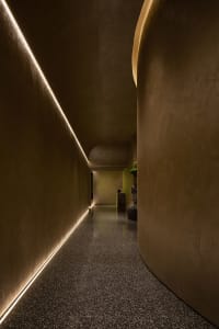 A modern, minimalist corridor with curved concrete walls and lit edges, featuring polished concrete floor.