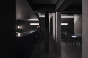 A minimalist restaurant interior with black concrete walls and lighting fixtures