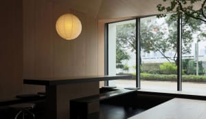 Minimalist modern restaurant interior with large windows, wooden seating and tables, and a lantern light hanging overhead.