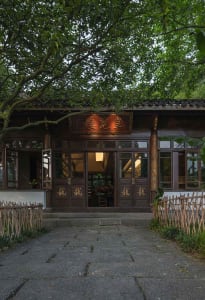 A traditional Chinese house with wooden exterior and tile roof, surrounded by lush greenery.