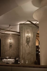 A modern restaurant with a concrete floor and stone walls, featuring elegant sconce lighting.