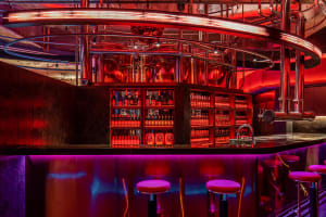 A modern industrial bar interior with metal and glass elements illuminated by neon lighting.