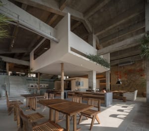 Industrial-style cafe interior featuring wooden tables, concrete ceiling, and exposed beams.