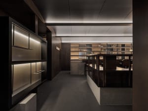 A modern restaurant bar with wooden interiors and shelves filled with bottles.