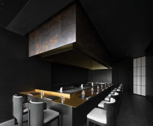 A sleek, modern restaurant interior featuring a black metallic bar counter and seating area.