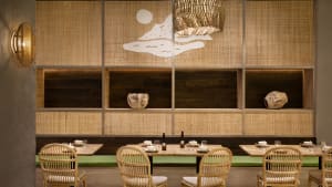 Restaurant interior with bamboo, wood, and fabric materials, featuring a wall display with a mountain and moon design.