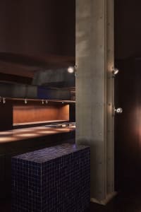 Industrial kitchen interior with a metallic counter, black tiled island, and metallic beams