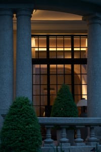 An elegant entrance adorned with classical columns and large glass windows, illuminated by warm lighting.