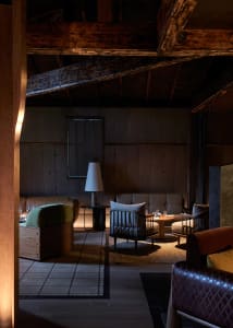 A cozy, industrial-style living room with wooden beams, dark wood furniture, and soft lighting features a comfortable seating