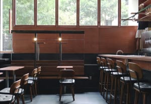 A modern cafe bar with wooden seating, leather stools, and metal accents.