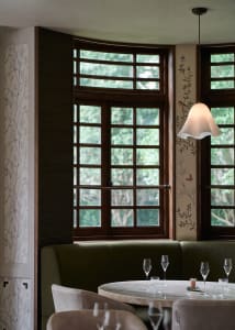 Modern restaurant interior with green booth seating, white marble table, and glass windows.