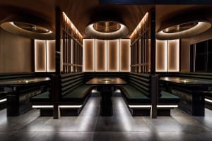 Modern restaurant booths with black leather seating, illuminated by warm, recessed lighting, and designed with sleek wood fur