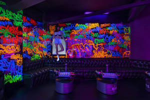 A vibrant nightclub room with colorful graffiti walls and black leather sofas.
