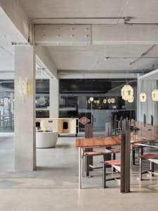 An interior view of a modern minimalist cafe with concrete walls, wooden tables, and hanging light fixtures.