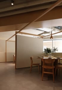 Modern coffee shop with wooden furniture and floor, featuring a dining table with cups and saucers, and a potted plant.