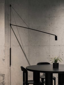 A black dining table and chairs against a concrete wall with a minimalist design.