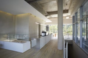 A minimalist coffee shop interior with concrete walls, light wooden flooring, and an industrial ceiling with exposed pipes.
