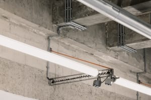 Lighting fixtures mounted on a concrete ceiling with exposed pipes and ducts.