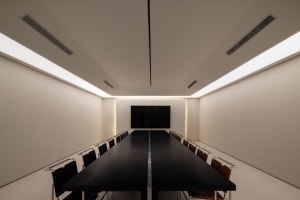 A minimalist conference room featuring a long black table and white walls.