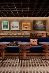 A well-lit, modern restaurant interior featuring blue velvet seating, carpet tiles, and framed artwork on the wall.