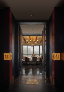 Modern, industrial-themed restaurant interior with marble flooring, large windows overlooking a cityscape, and a warm, inviti