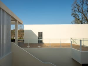 A minimalist modern rooftop deck with wooden flooring and white walls, under a clear blue sky.