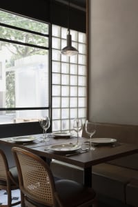 Aesthetically minimalist restaurant interior with wood tables, concrete walls, frosted glass block windows, and modern lighti