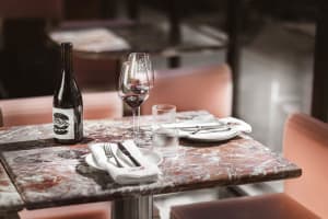 Marble countertop in an industrial-style restaurant with wine glasses, a wine bottle, and tableware.