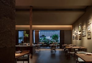 A modern restaurant interior featuring wooden tables, stone details, and green plants.